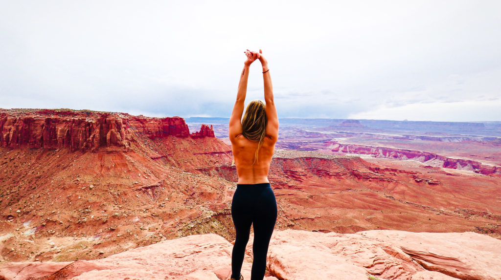 Briana standing topless in the desert with her back facing the camera with a view of canyonlands national park in the distance