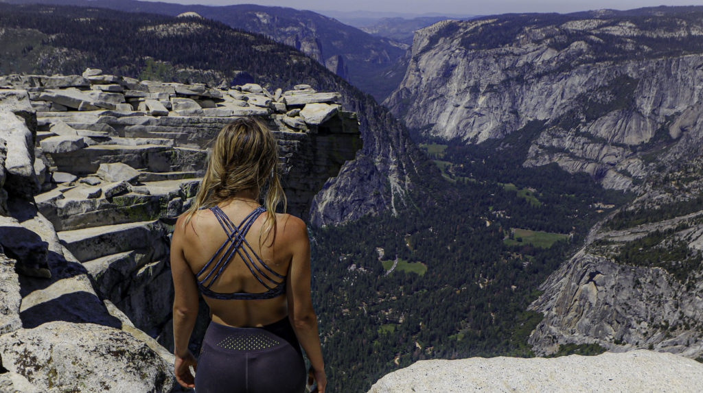 Briana, with her back facing the camera, standing at the top of half dome. Overlooking the grand view.